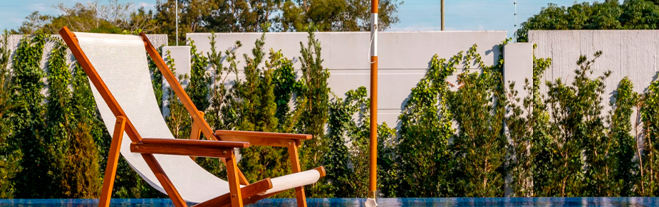 espregui&ccedil;adeira de madeira com assento branco repousa calmamente &agrave; beira de uma piscina de &aacute;guas azuis profundas, emoldurada por uma parede texturizad